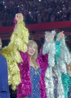 two women in sequins are holding their hands up to the sky at a concert