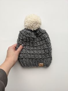 a hand is holding a gray and white knitted beanie with a pom - pom on top