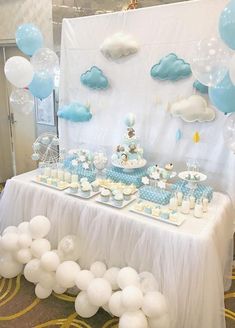 a table topped with lots of white and blue desserts next to balloons in the shape of clouds