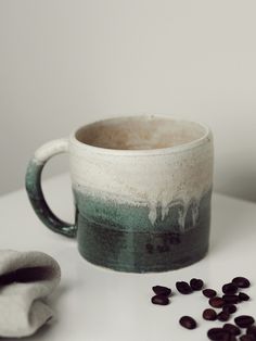 a coffee cup sitting on top of a white table next to some black and green beans