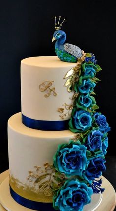 a three tiered cake with blue flowers and a peacock on top