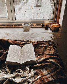 an open book sitting on top of a bed next to a cup of coffee and candle