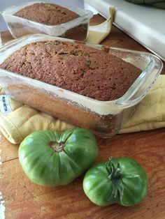 two green tomatoes and a loaf of bread on a wooden table next to each other