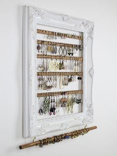 a white frame holds several pairs of earrings and other jewelry hanging on it's wall