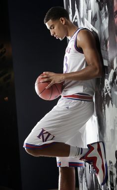 a young man holding a basketball standing next to a wall with pictures on the walls