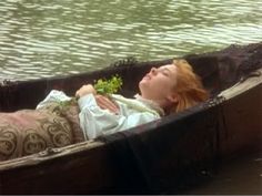 a woman laying in a boat on the water with her eyes closed and holding a plant