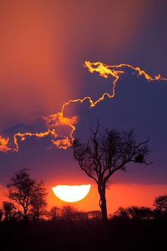 the sun is setting behind some trees and clouds