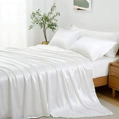 a bed with white sheets and pillows in a bedroom next to a plant on a nightstand