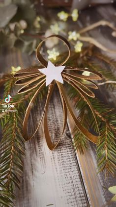 an ornament made out of gold ribbon and white star on top of pine branches