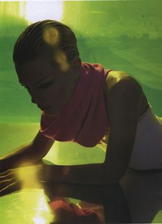 a woman in pink shirt and white shorts leaning over a glass table with water behind her