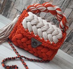 an orange and white handbag sitting on top of a wooden floor next to a tassel