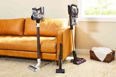 two vacuums sitting on the floor next to a couch