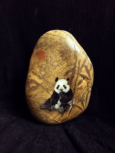a panda bear sitting on top of a rock with bamboo leaves painted on it's side