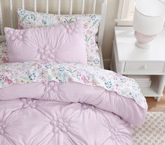 a bed with pink comforter and pillows in a room next to a night stand