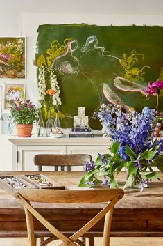 a wooden table topped with purple flowers next to a chalkboard covered in pictures and paintings