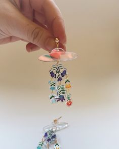 a hand is holding a glass wind chime in front of another one with flowers on it