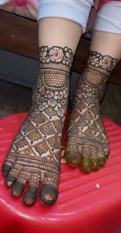 the feet are decorated with henna on top of a red suitcase in front of a woman's legs