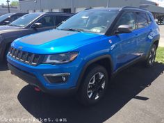 a blue jeep is parked in front of other cars at a dealership on a sunny day