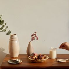 a table topped with two vases filled with flowers next to a bowl of cereal