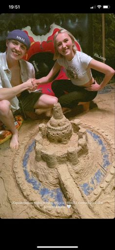 two people sitting on the ground next to a sand sculpture