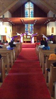 people sitting in pews at the end of a church with red carpet and stained glass windows