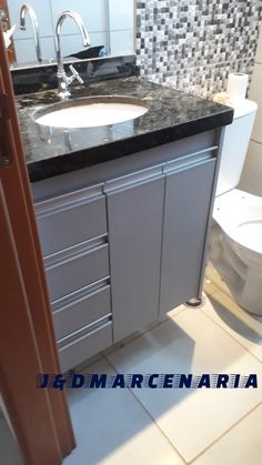 a white toilet sitting next to a sink in a bathroom under a vanity with black counter top