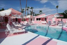 a pool with chairs and umbrellas next to a pink house that has been painted in shades of pink