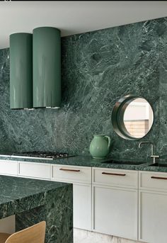 a kitchen with green marble counter tops and white cabinets, along with a round mirror on the wall