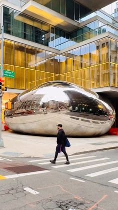 a man walking across a street in front of a giant silver object that says new york city now has its own bean