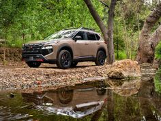 the new nissan pathfinder suv is parked in front of some trees and rocks near a body of water