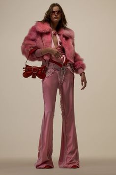 a woman in pink pants and fur coat holding a handbag while standing next to a white wall