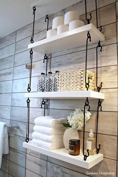 bathroom shelving with white towels and candles on shelves next to toilet paper rolls, soap dispenser and towel rack