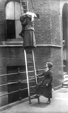 a woman standing on top of a ladder next to a building