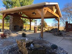 an outdoor covered patio area with rocks and gravel around the fire place, trees in the background