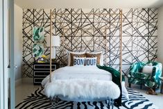 a white bed with black and white designs on the wall behind it in a bedroom