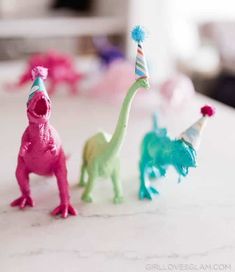 three toy dinosaurs with party hats on their heads, one is pink and the other is green