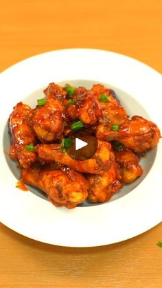 a white plate topped with chicken wings covered in sauce and garnished with green onions