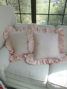 three pink pillows on a white couch in front of a large window with trees outside