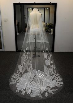 a wedding veil with flowers and leaves on it is displayed in front of a doorway