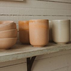 three bowls and two cups sitting on a shelf