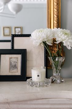 a vase filled with white flowers sitting on top of a table next to a candle