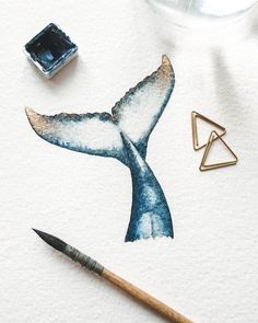 a watercolor painting of a blue whale tail next to a paintbrush and some ink