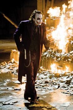 the joker is standing in front of a fire