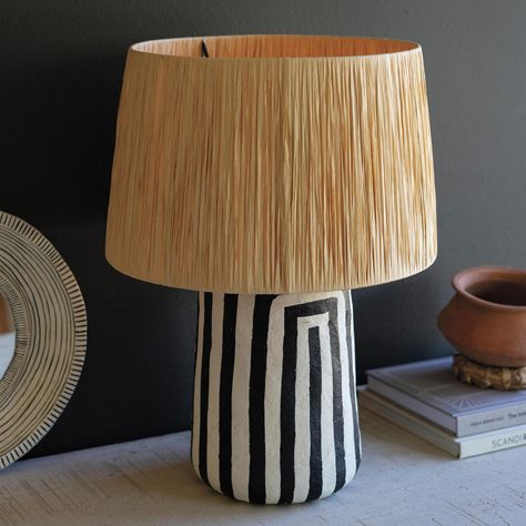 Discover the unique charm of this paper-mâché table lamp, topped with a raffia shade. Perfectly designed to illuminate a dark corner, it stands at an elegant 18.5 in height and showcases the artistry of Indian craftsmanship. Whether placed in neutral or colorful boho-inspired spaces, this lamp serves as a bright and delightful addition. Accommodates a 40-watt bulb (not included). The convenient toggle (on/off) switch is thoughtfully located on the black cloth cord. Maintain its beauty with a sim Paper Mache Table, Beach House Lamp, Justina Blakeney Jungalow, Black White Table, Black And White Paper, House Lamp, Wood Fuel, Justina Blakeney, Colorful Space