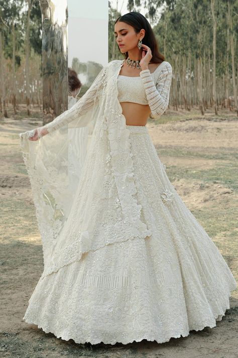 Ivory lehenga with all-over floral embroidered motifs and cutwork hem. Comes with embroidered blouse and organza dupatta. Component: 3 Pattern: Embroidery Type Of Work: Silk Threads, Pearl, Beads, Cutdana and Sequins Neckline: Square Sleeve Type: Full Fabric: Organza and Tulle Color: Ivory Other Details:  Embroidered dupatta with cutwork border Low back with tie up and tassels Sleeves with striped panels Occasion: Bride - Aza Fashions Ivory Lehenga, Wedding Lenghas, Tulle Blouse, Ridhi Mehra, White Lehenga, Full Sleeve Blouse, Tulle Embroidery, Organza Lehenga, Lehenga Blouse Designs