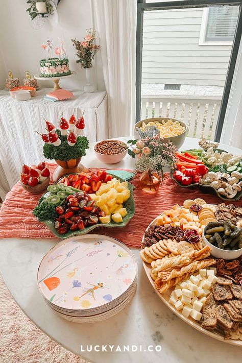 Looking for fairy-themed party food ideas for your kid's birthday? Look no further! Create an enchanting garden table with strawberry mushrooms, fruit platters, veggie platters with hummus/dip, a cheese and cracker board, salads, and cheese sliders. Don't forget the chips, pretzels, and applesauce pouches. And of course, there's a magical theme cake for dessert too. Get inspired by reading our blog post! Lucky Andi. Fairy Birthday Party: Food Ideas Fairy Birthday Food Table, Fairy Garden Snacks, Fairy Birthday Party Snacks, Woodland Fairy Food Ideas, Fairy Themed Snacks, Fairy Garden Brunch, Fairy Birthday Cake Table, Fairy Birthday Dessert Table, Fairy Birthday Party Ideas Activities