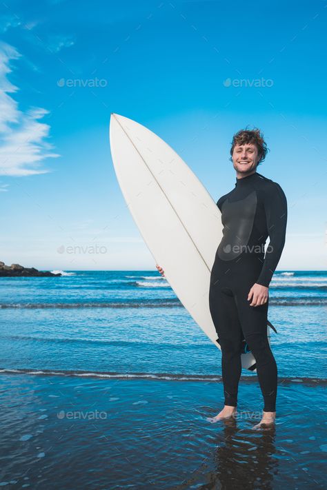 Surfer standing in the ocean with his surfboard. by megostudio. Young surfer standing in the ocean with his surfboard in a black surfing suit. Sport and water sport concept. #Sponsored #megostudio, #Young, #surfer, #surfboard Man With Surfboard, Holding Surfboard Pose, Surfer Pose Reference, Surfer Reference, Beach Reference Pose, Surfing Pose Reference, Surfing Reference, Surfing Pose, Surfer Suit