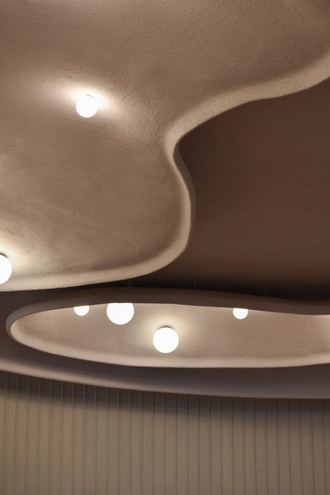 Its curved lines are echoed in the false ceiling overhead, where globe-shaped lights are positioned like pearls within oyster-shaped reliefs made from textured lime plaster. Wooden Panelling, Counter Seating, Plaster Ceiling, Subtle Luxury, Faux Plafond, Ceiling Detail, Curved Walls, Terracotta Tiles, False Ceiling Design