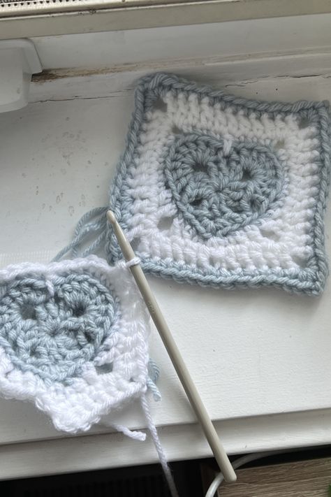 One completed crocheted granny square on the upper right corner with a blue heart in the center white rounds around and a blue trim. Lower left has the same granny square incomplete with the hook still in it. Tela, Heart Shaped Granny Square, Granny Square Heart Pattern, Heart Granny Square Pattern Free, Crochet Sweater For Beginners, Crochet Heart Granny Square, Granny Square Heart, Heart Granny Square, Cardigan Tutorial