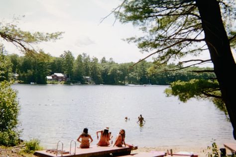 Image is of a lake. There are a few people sitting by the lake on beached docks and a few people in the water. Summer Camp 80s Aesthetic, 90s Summer Camp, 80s Summer Camp Aesthetic, American Summer Aesthetic, Vintage Summer Camp, American Summer Camp, Lake Core, Summer Camp Aesthetic, Camp America